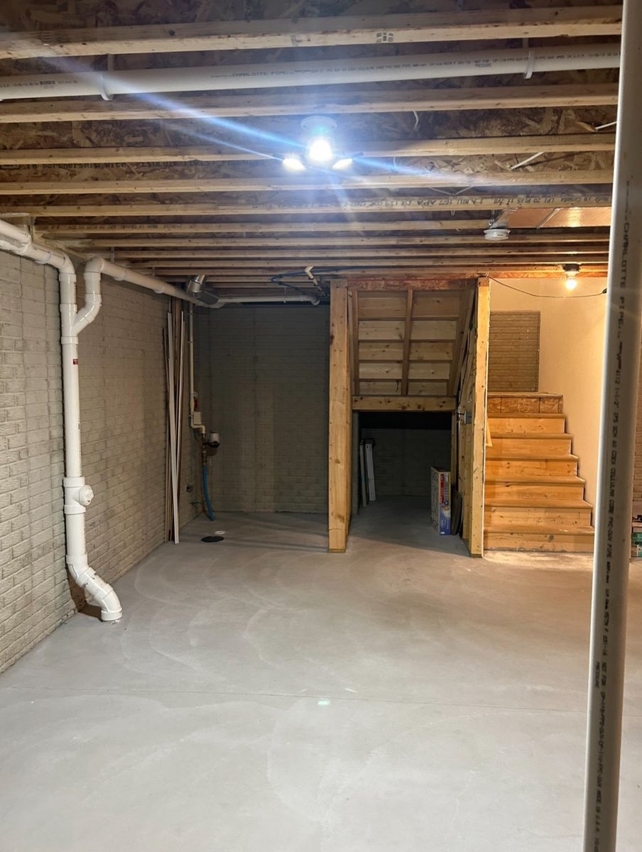 Unfinished basement with bare block walls and open joists before the finishing work began