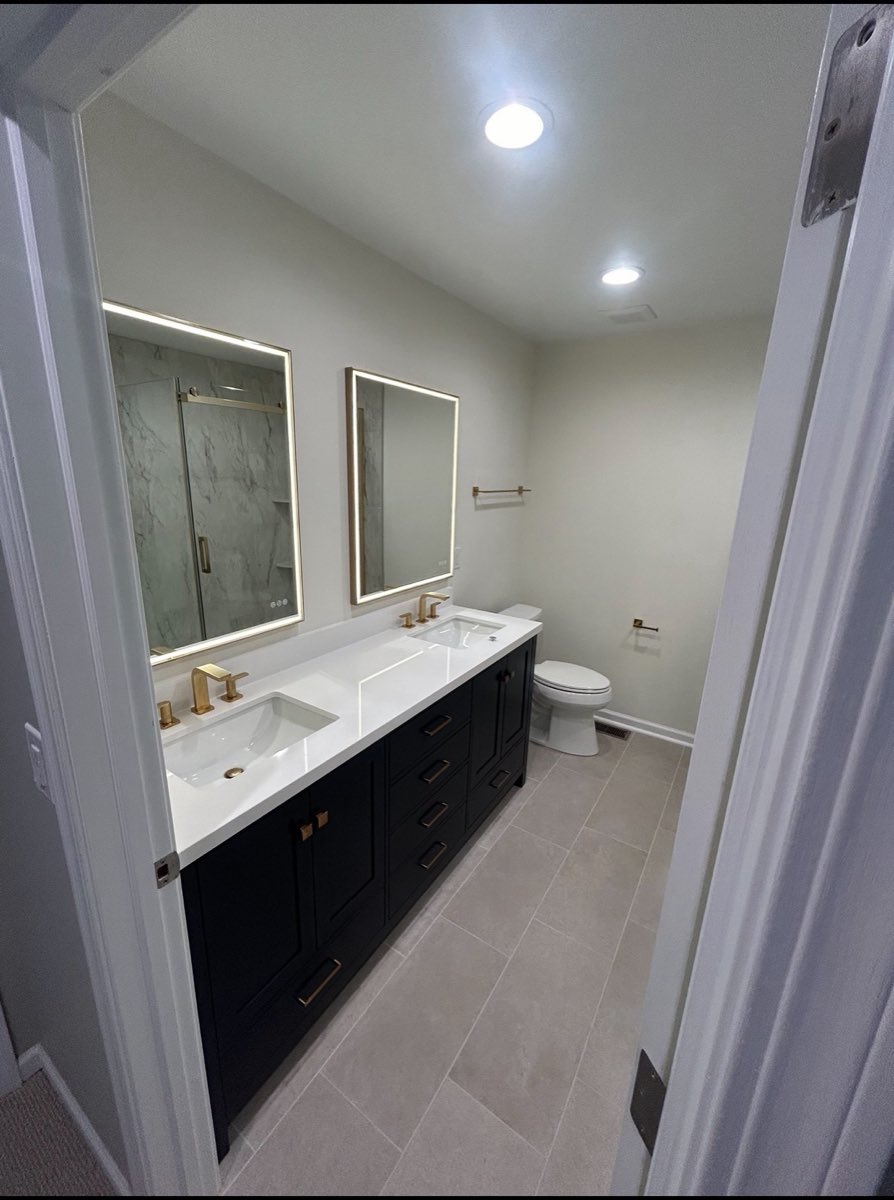 Remodeled bathroom with a navy double vanity, backlit LED mirrors and brushed-gold fixtures