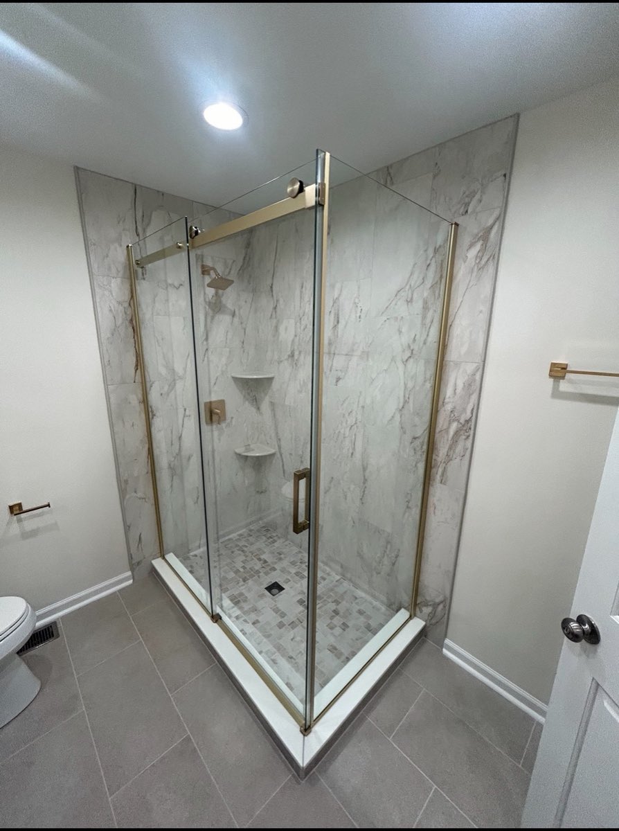 Frameless glass corner shower with marble-look wall tile, a mosaic shower pan and brushed-gold trim