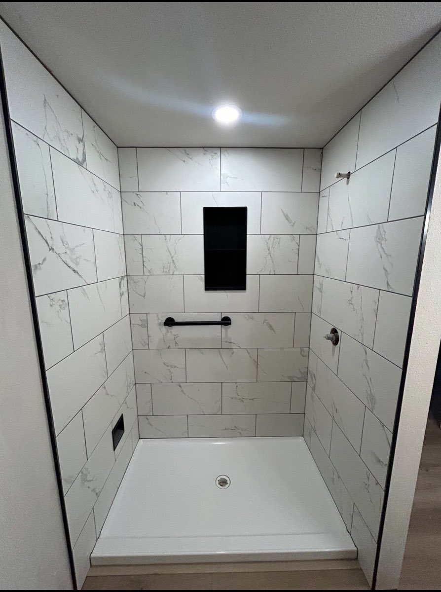 Large-format marble-look tile shower with a black recessed niche and matte-black fixtures