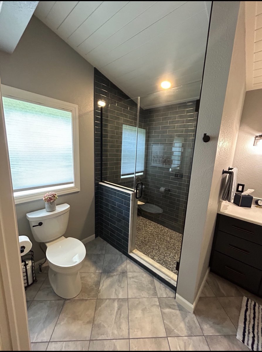 Walk-in shower with slate-blue subway tile, a pebble stone shower floor and large-format tile flooring
