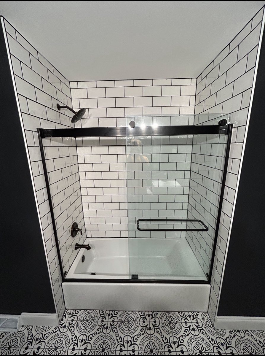 Tub and shower remodel with white subway tile, a black sliding glass door and patterned floor tile