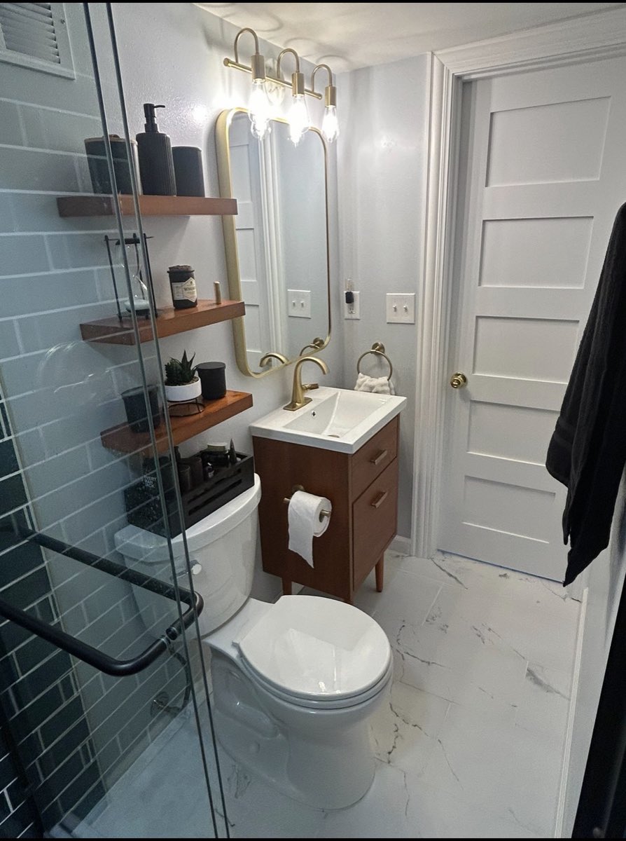 Compact bathroom remodel with a walnut vanity, brushed-gold fixtures and a marble-look tile floor