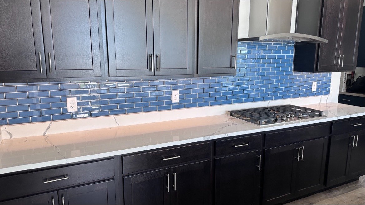 Kitchen remodel with a blue glass tile backsplash, dark shaker cabinets and quartz countertops