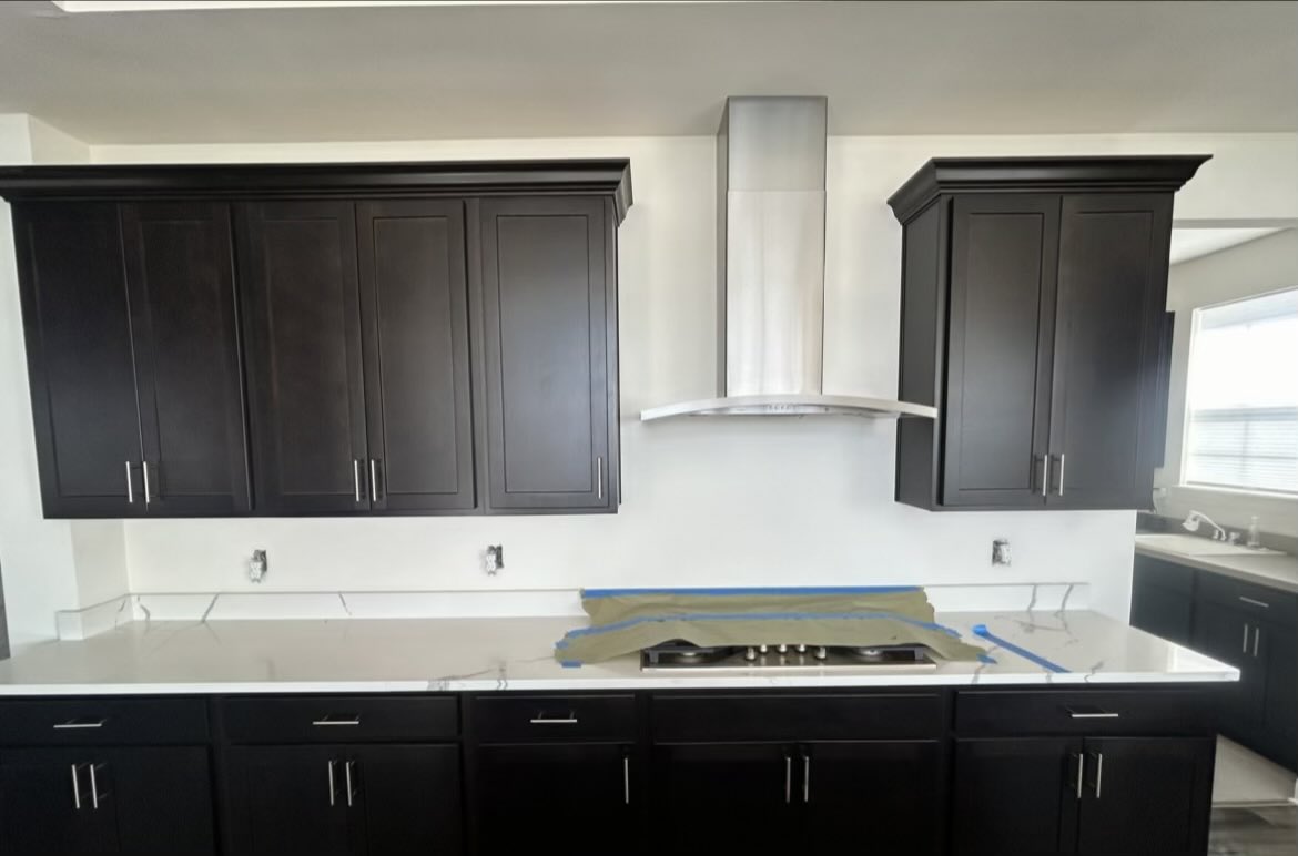 Kitchen with dark shaker cabinets, white quartz countertops and a stainless range hood